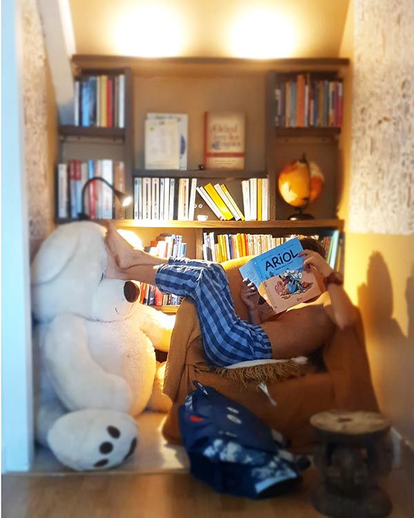 enfant assis dans un fauteuil qui lit un livre devant une bibliothèque